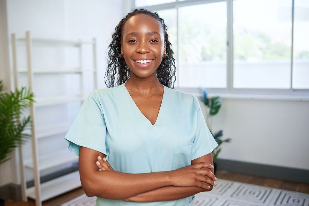 Smiling woman in a light blue top standing with arms crossed in a bright office.