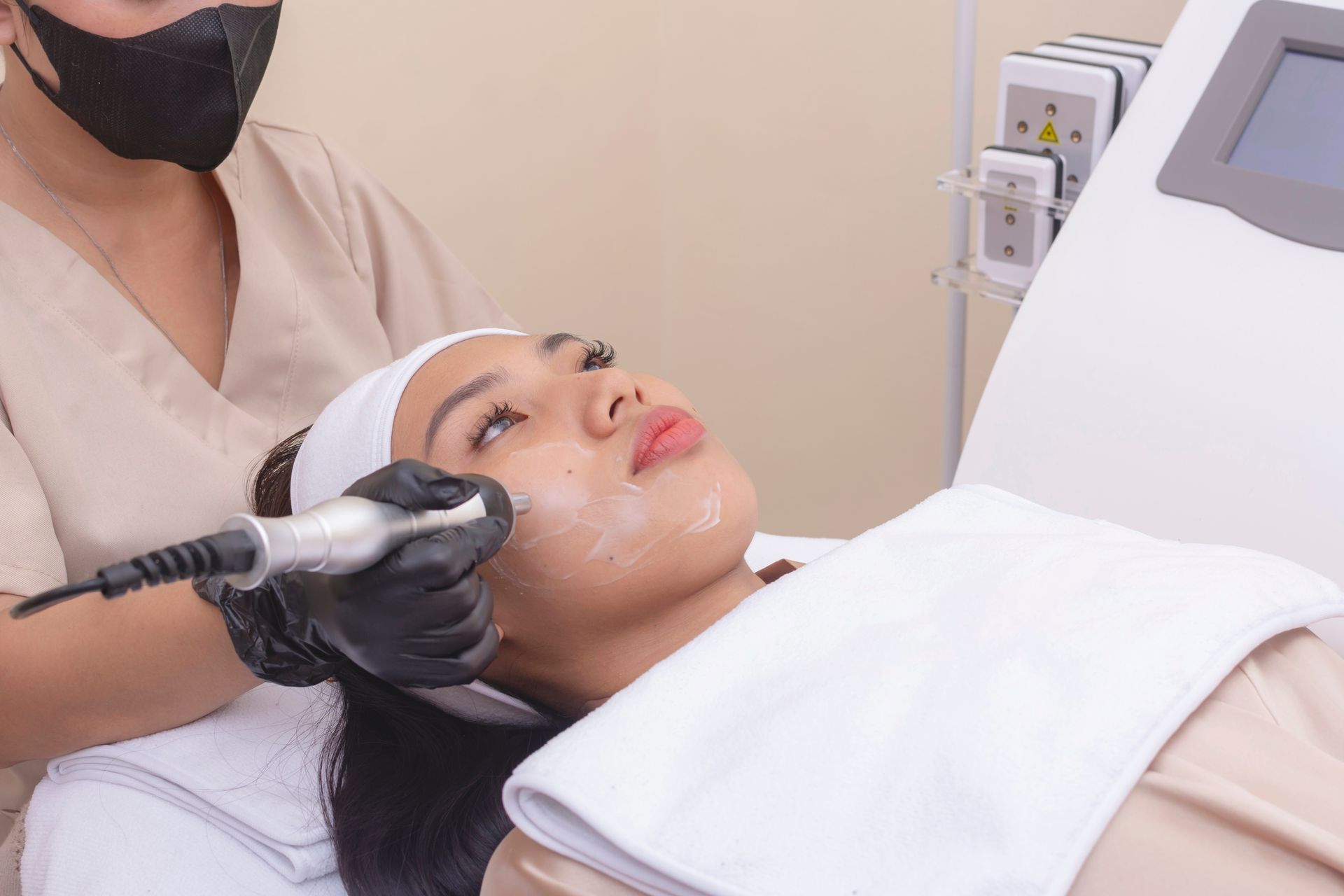 Facial treatment in progress as a clinician applies a device to a reclining patient’s cheek.