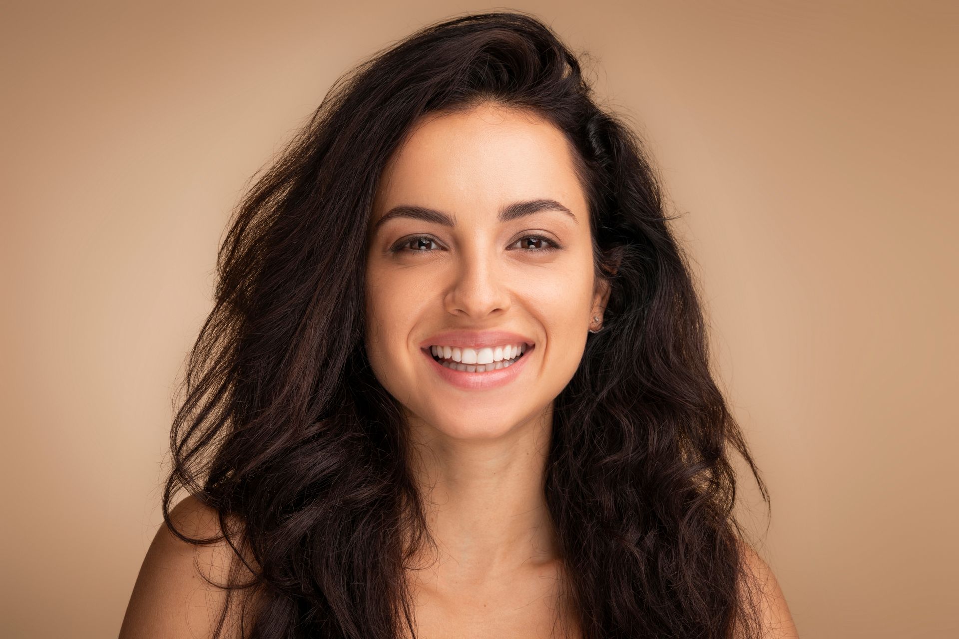 Smiling woman with dark wavy hair against a beige background