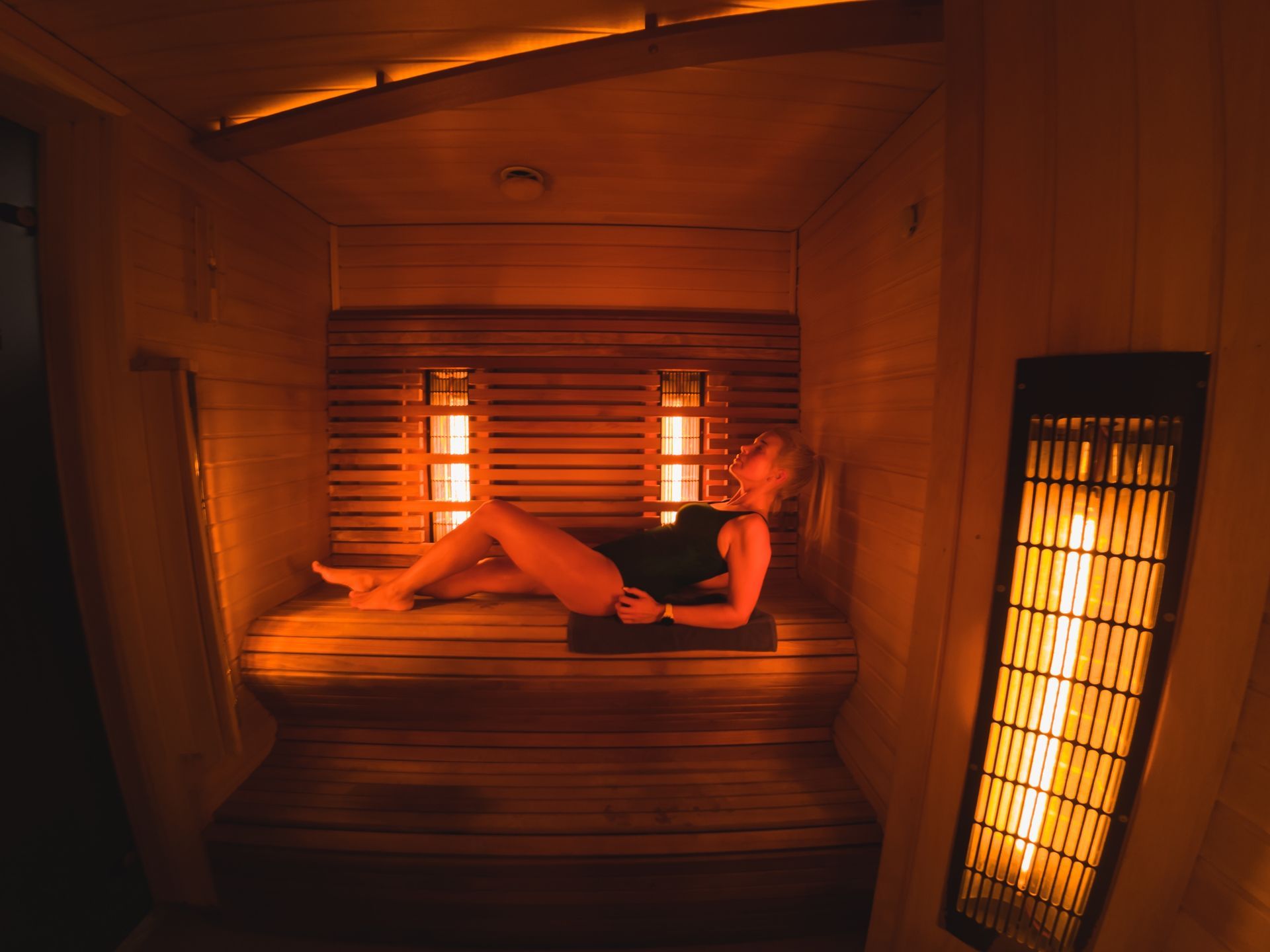 Person reclining in a wooden sauna lit by warm orange heaters
