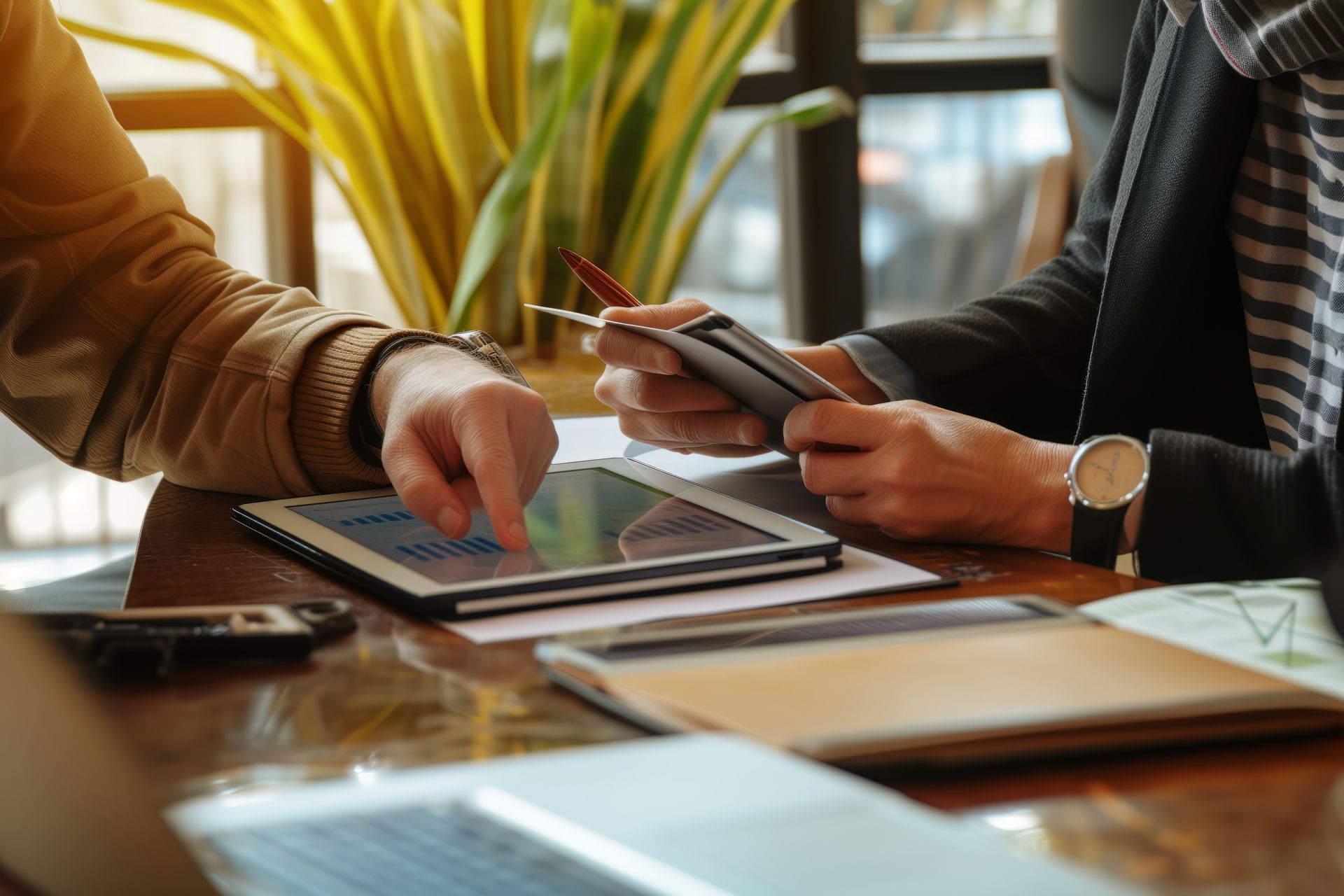 Two people collaborating at a table with a tablet, smartphone, and laptop in a bright office setting