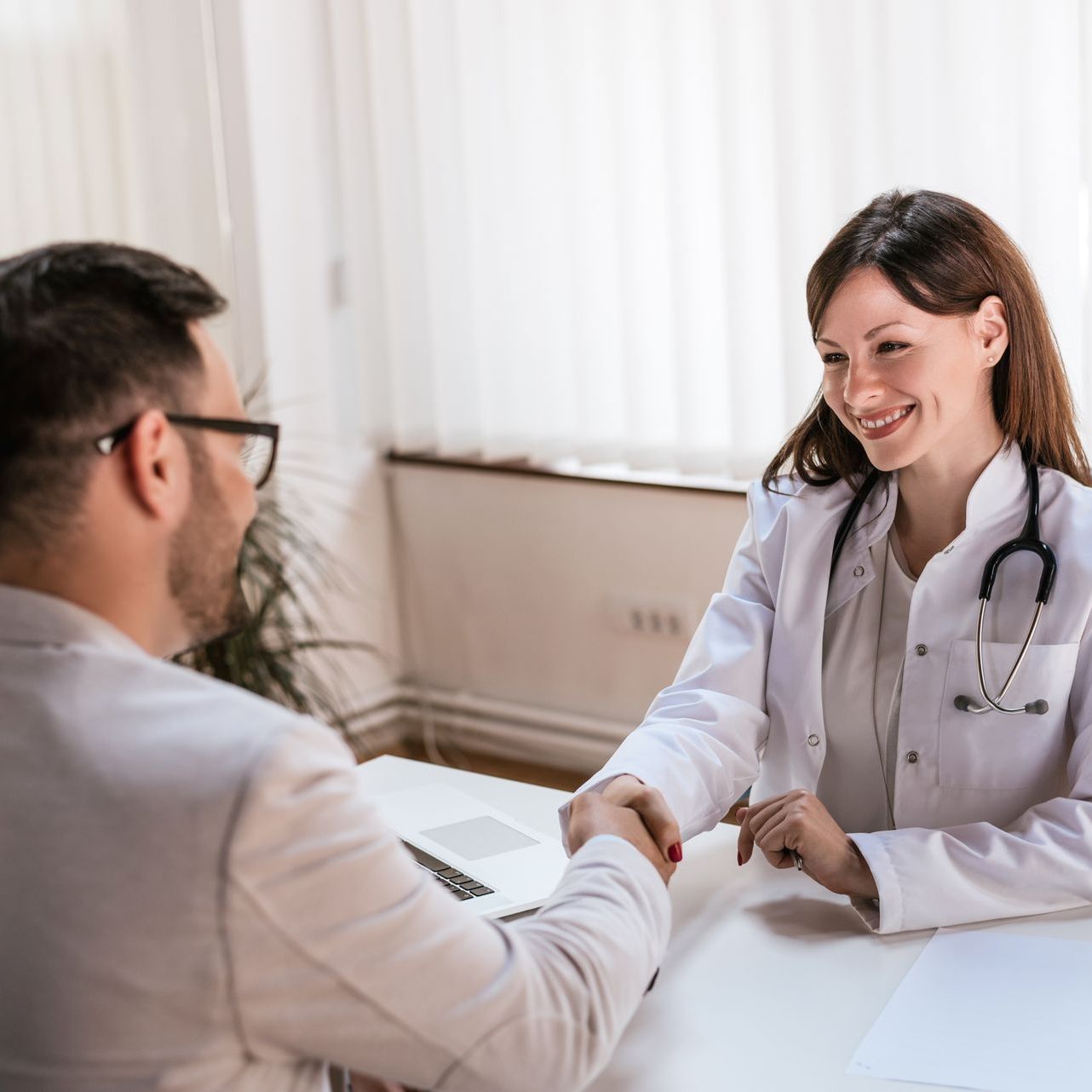Doctor smiling and shaking hands with a patient in a bright clinic office