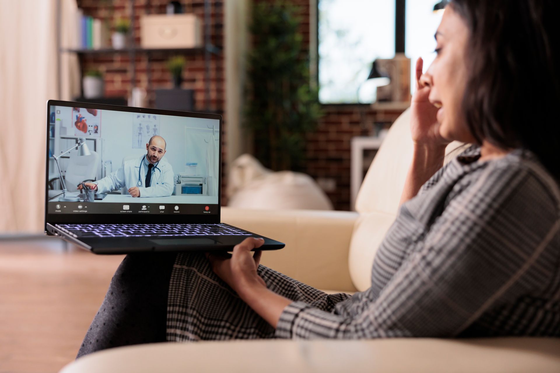 Woman on a couch using a laptop for a video call with a doctor