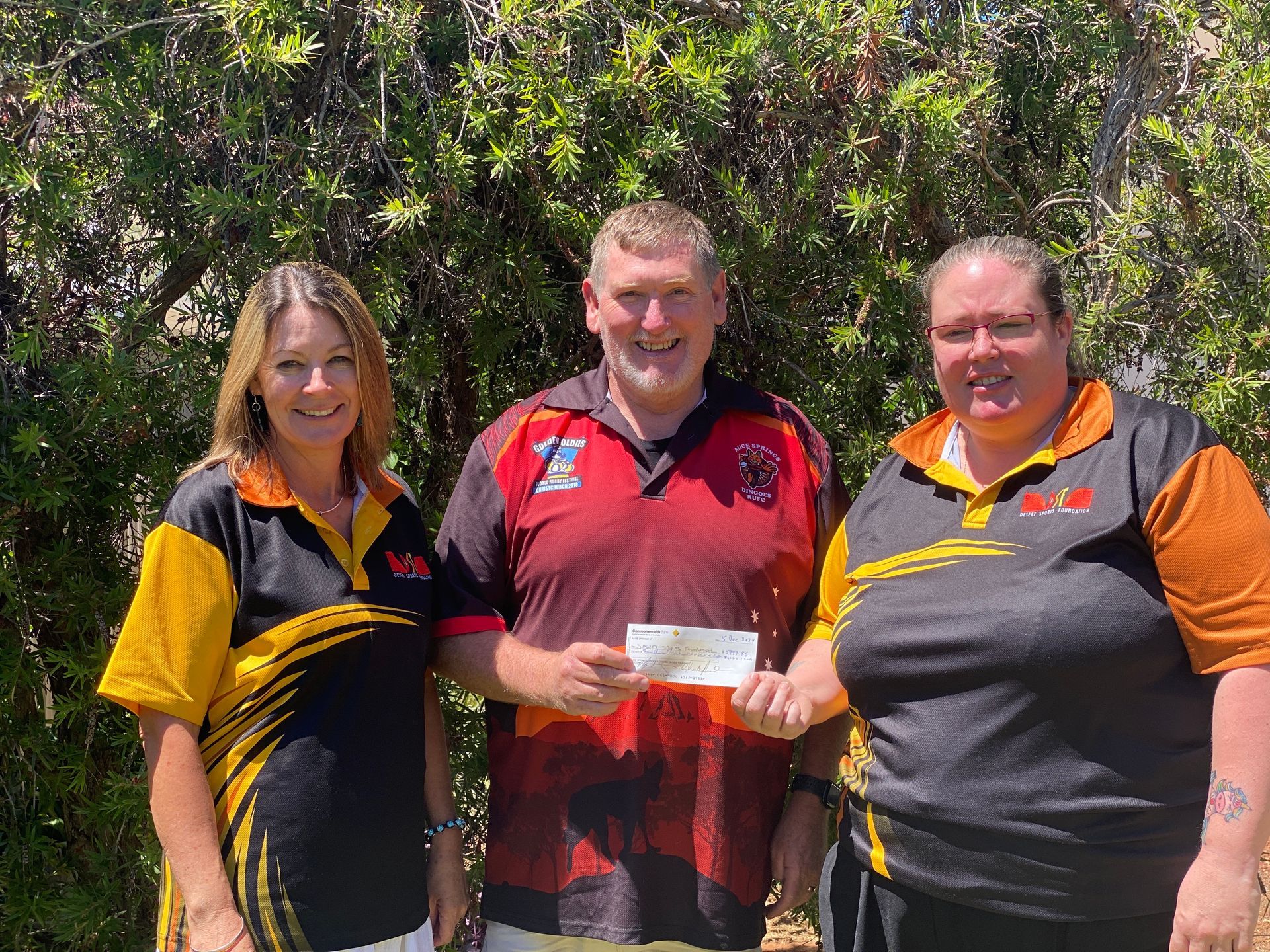 A man and two women are standing next to each other holding a check.