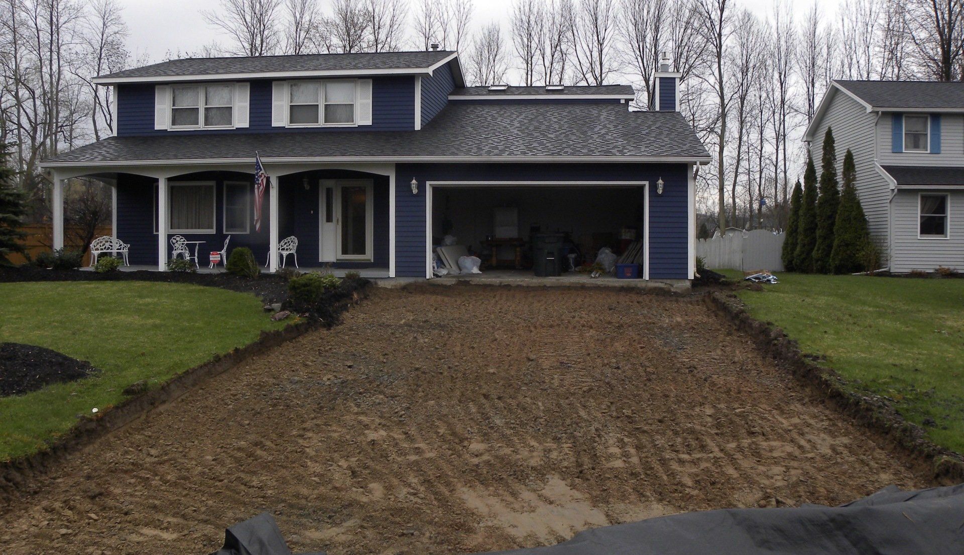 Driveway under construction in front of a blue two-story house with a garage and green lawn.