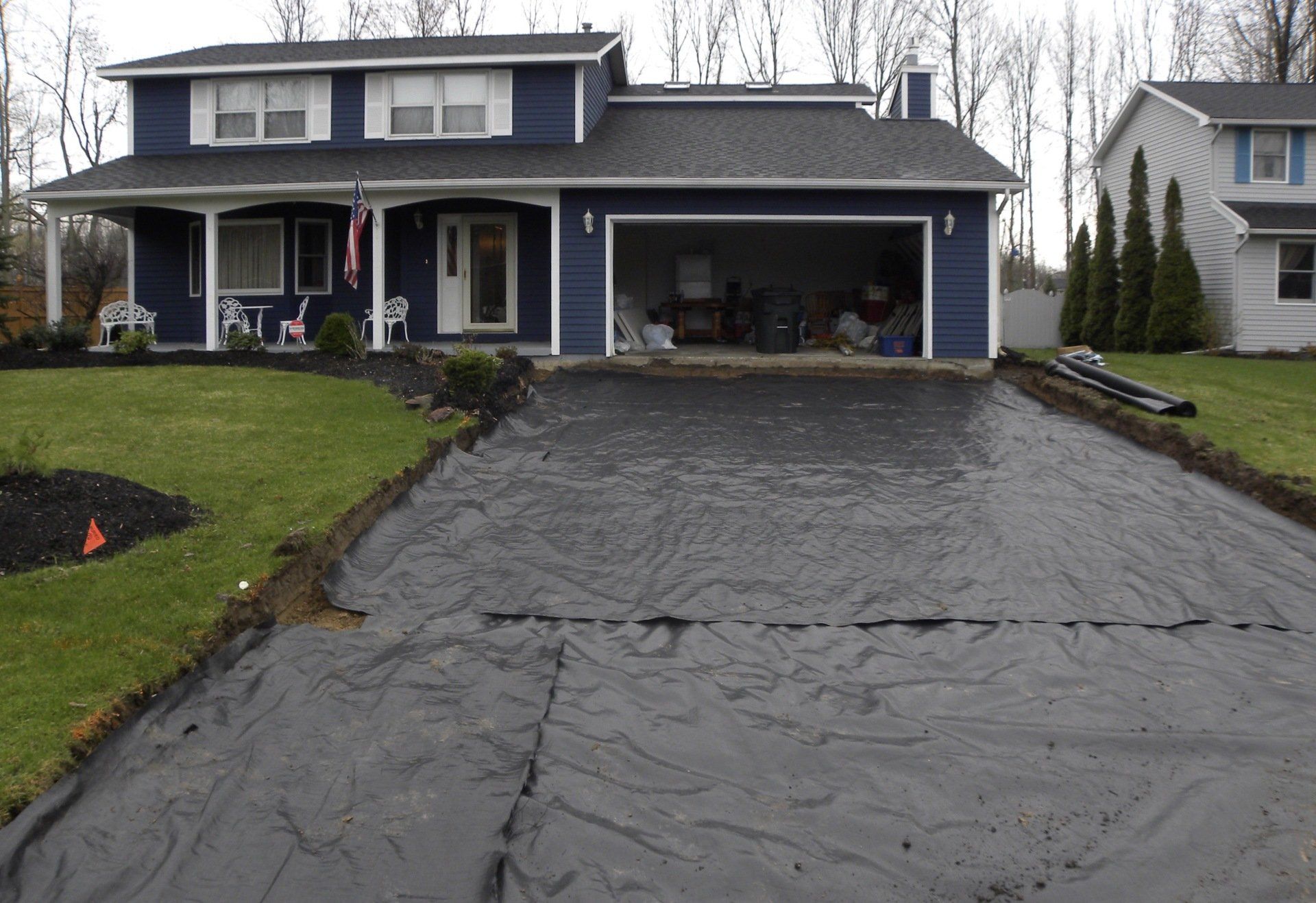 Dark blue house with black tarp covering the driveway, awaiting landscaping.