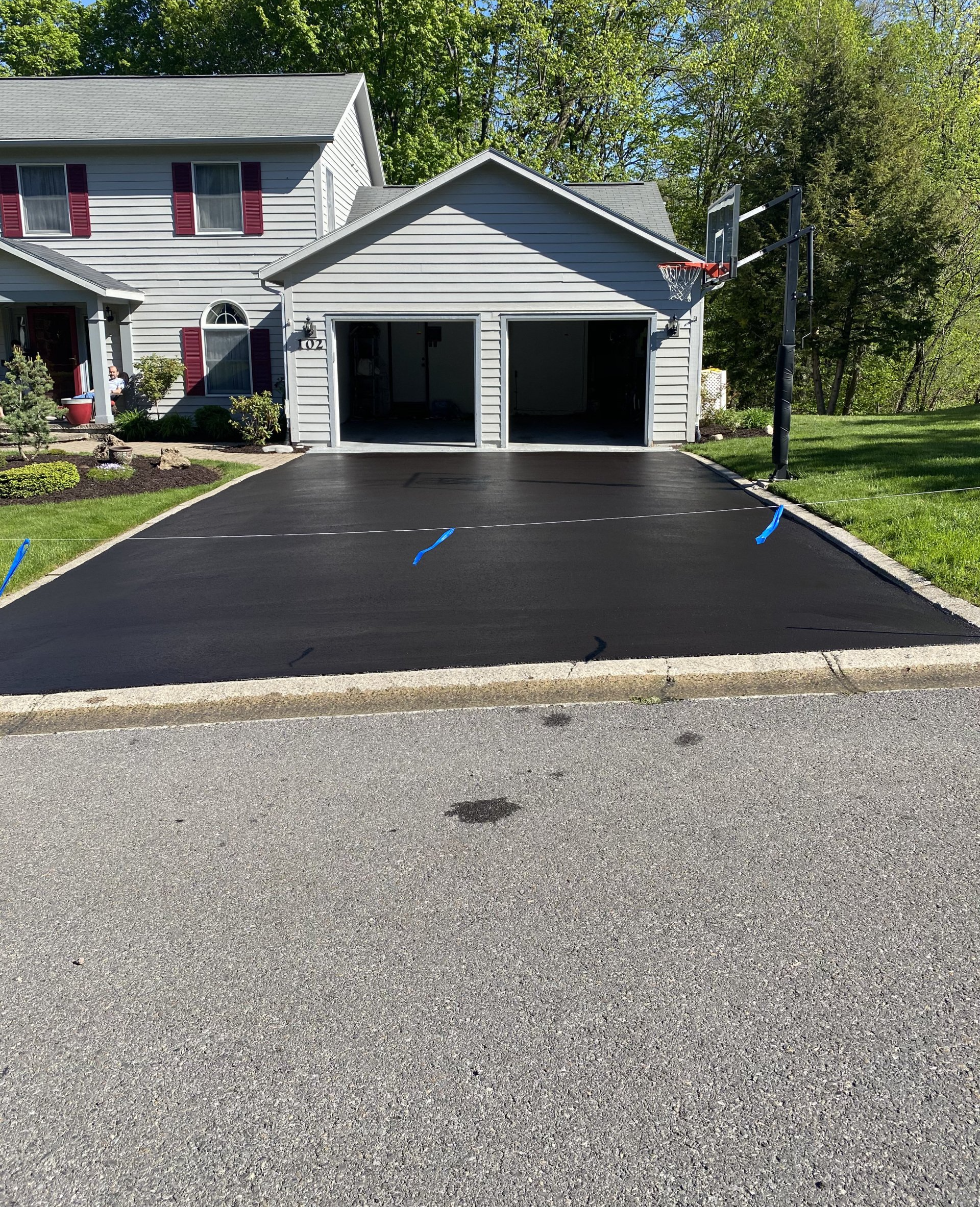 Freshly paved black driveway in front of a gray house and garage with a basketball hoop.