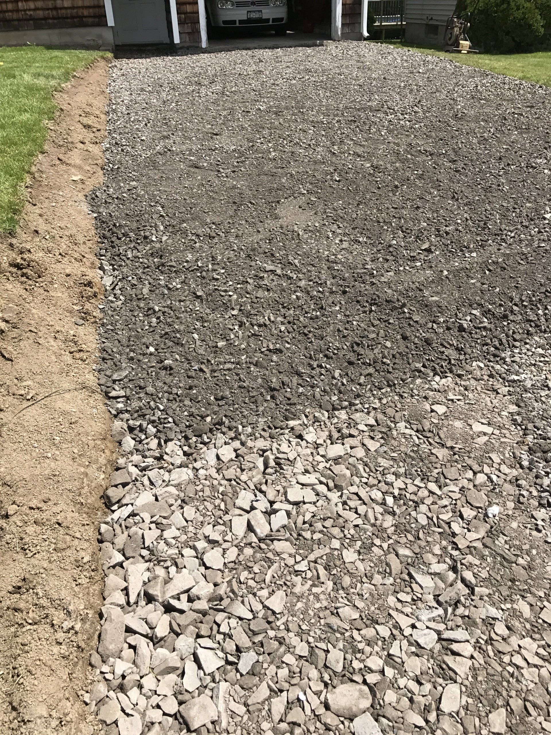 Gravel driveway next to a strip of dirt and grass, leading to a garage.
