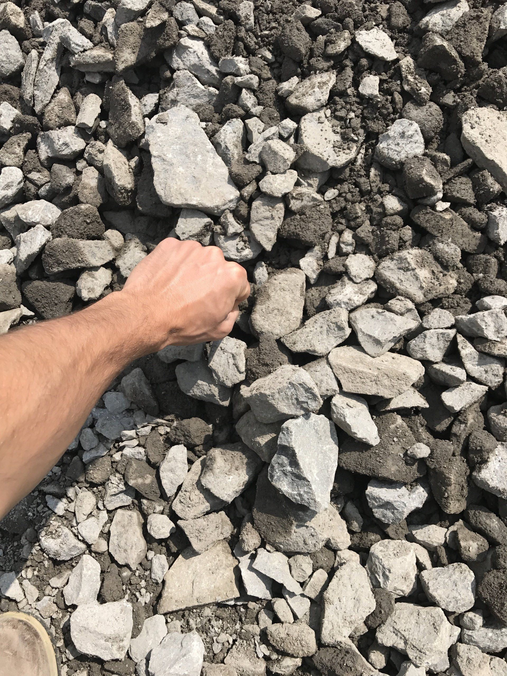 Hand touching pile of broken concrete, varying shades of gray, outdoors.