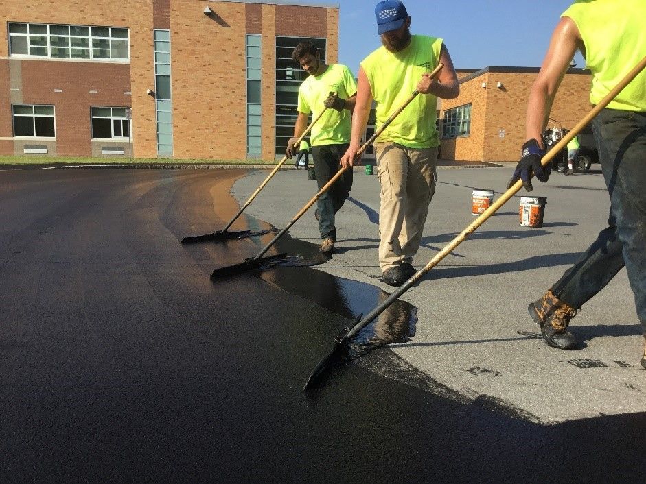 Men in yellow work clothes sealcoating a parking lot.