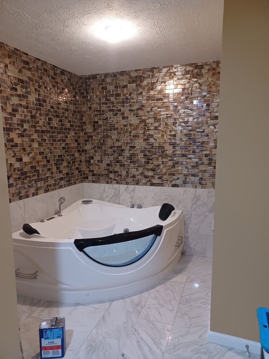 White corner jacuzzi tub in a bathroom with mosaic tile walls and marble floors.