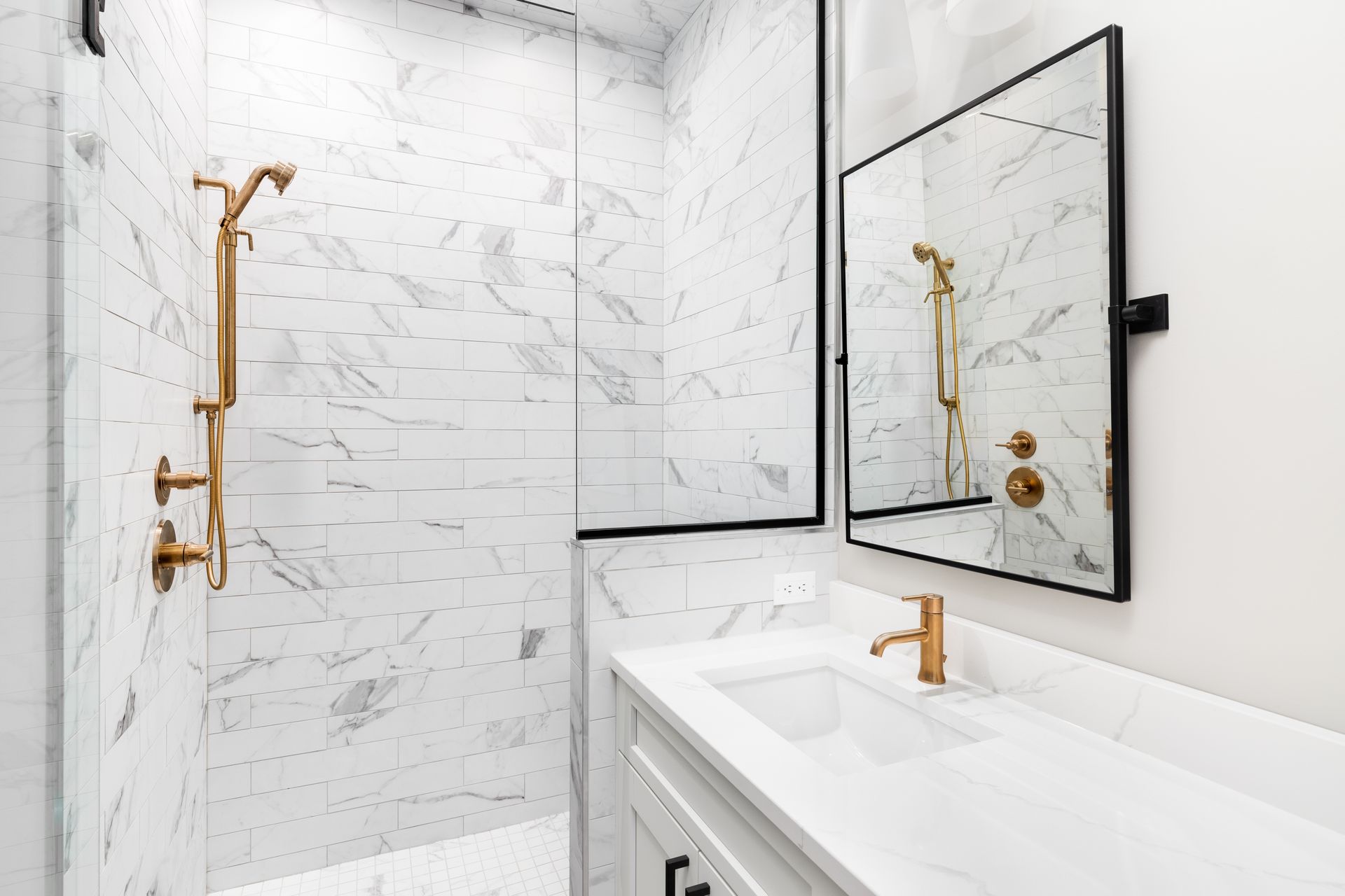 Bathroom with marble tile shower, gold fixtures, and white vanity with a mirror.