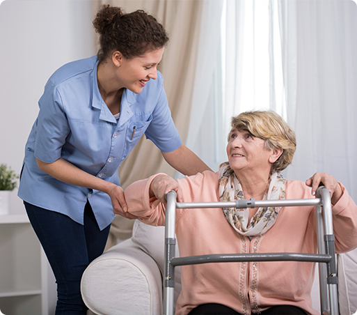 Caregiver assisting a woman using a walker. Woman seated on a couch, smiling. Light blue shirt, beige top.