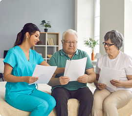 Caregiver showing paperwork to two seniors indoors.