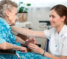 A healthcare worker assists a person sitting on a bed, supporting their leg and foot.