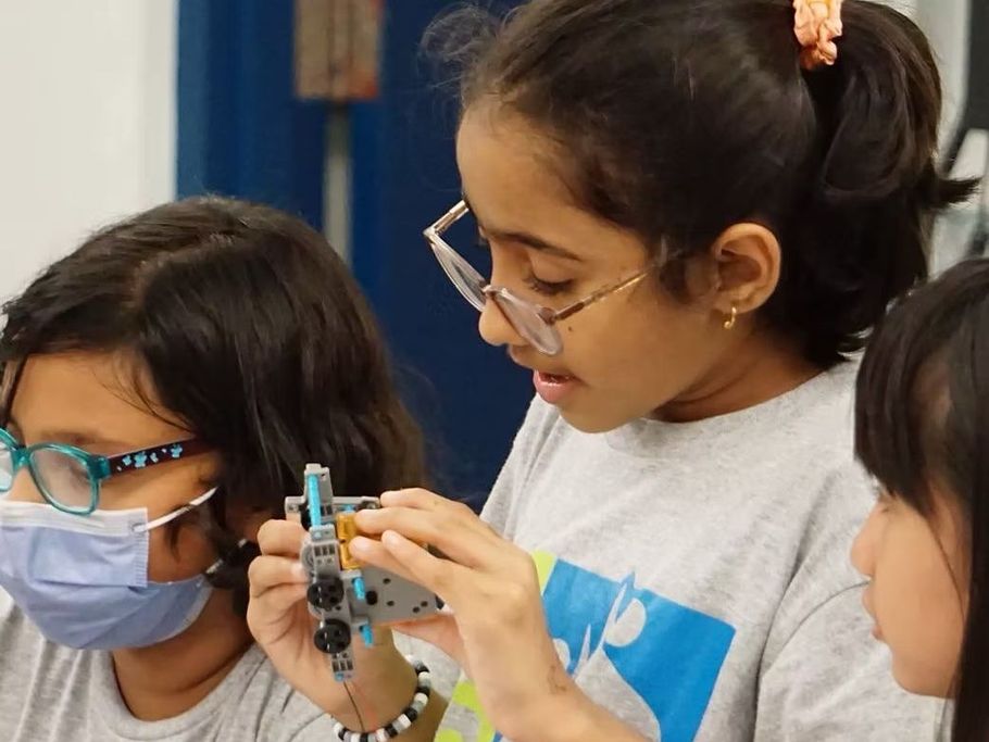A group of young girls wearing masks and glasses are working on a robot.