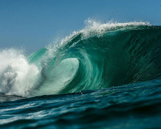 A large, turquoise ocean wave crests and curls, with white foam.