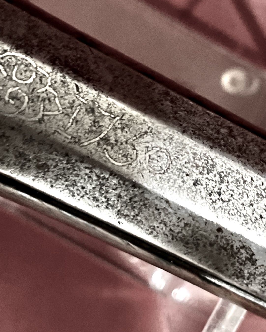Close-up of a tarnished metal object with etched text and decorative flourishes along the edge.
