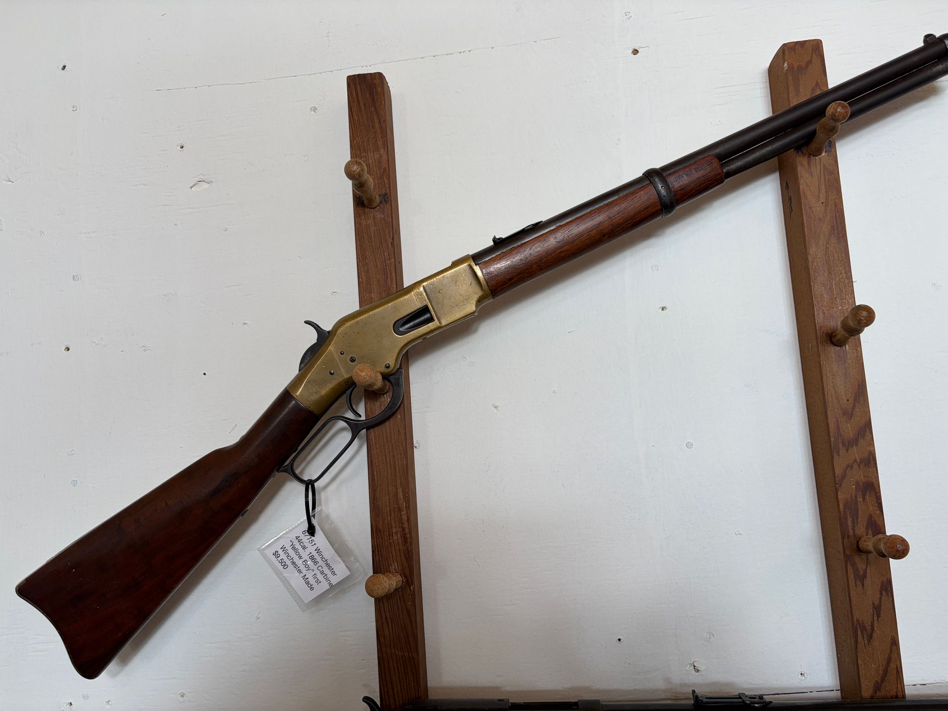 Long rifle with wooden stock and brass receiver mounted on a wooden wall display stand