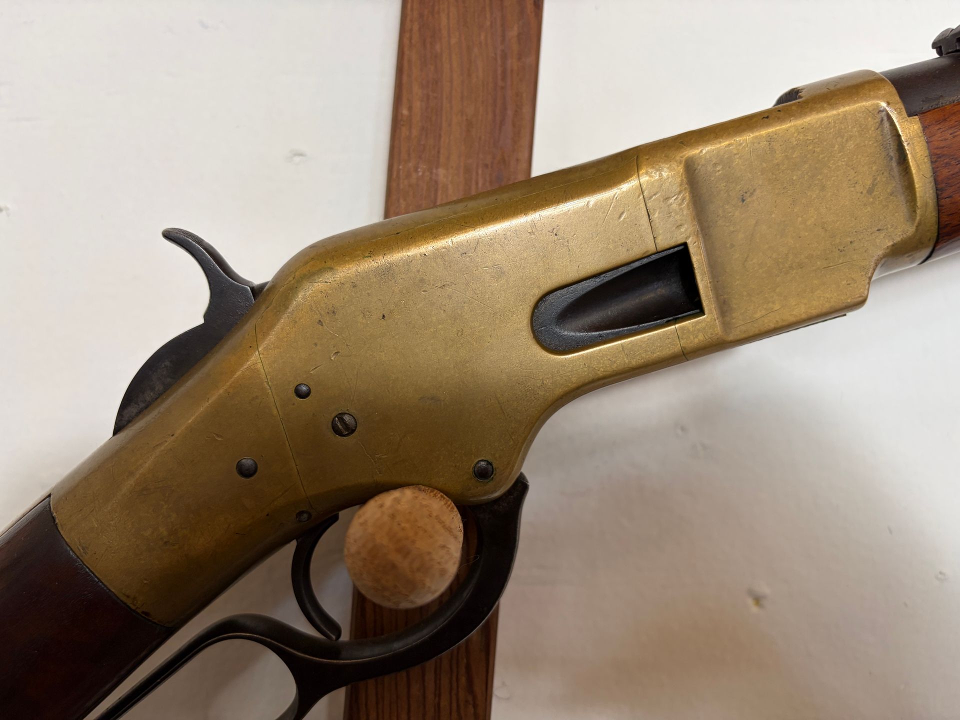 Long rifle with wooden stock and brass receiver mounted on a wooden wall display stand