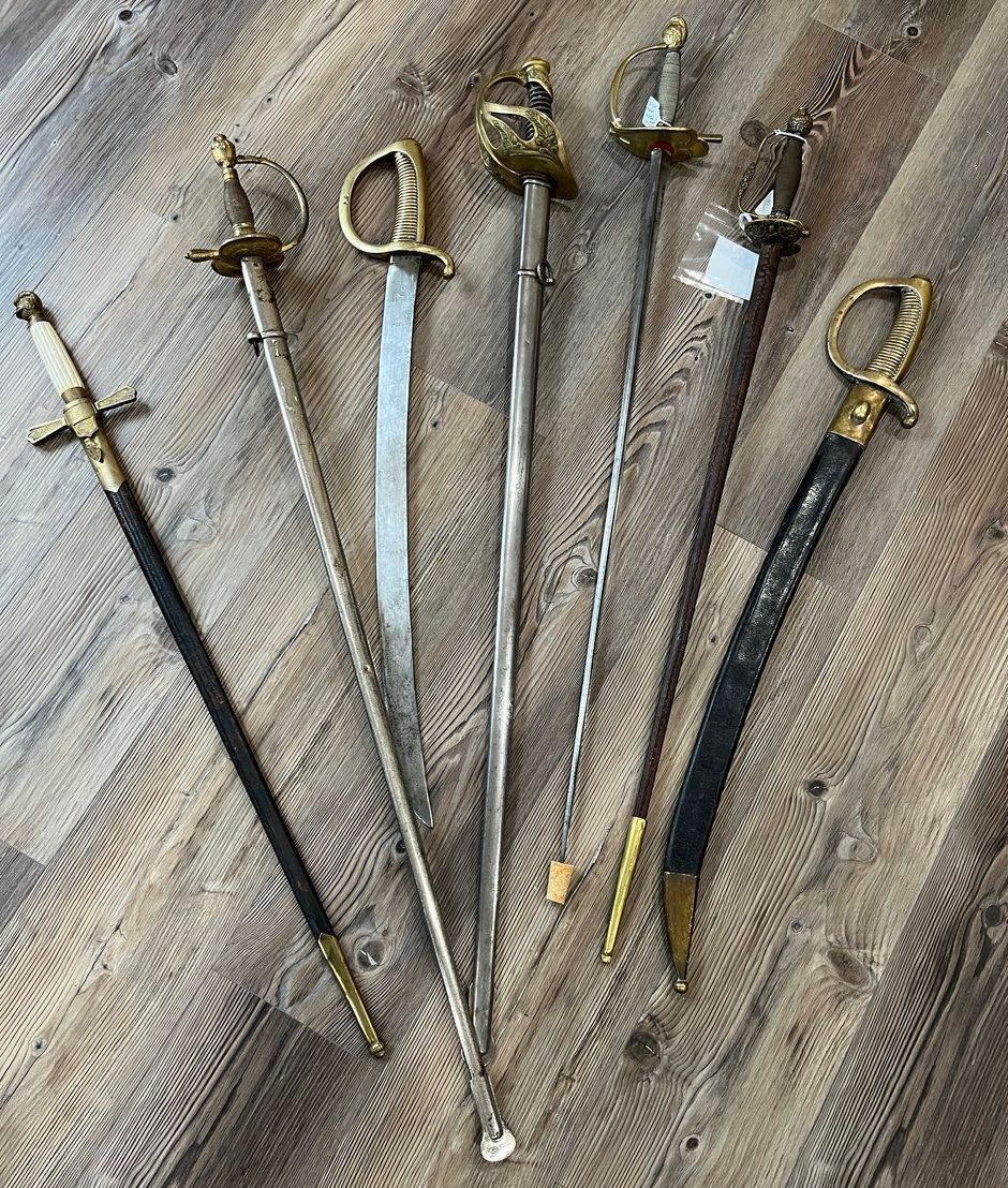 Six antique swords of various designs, displayed on a wood-grain surface.