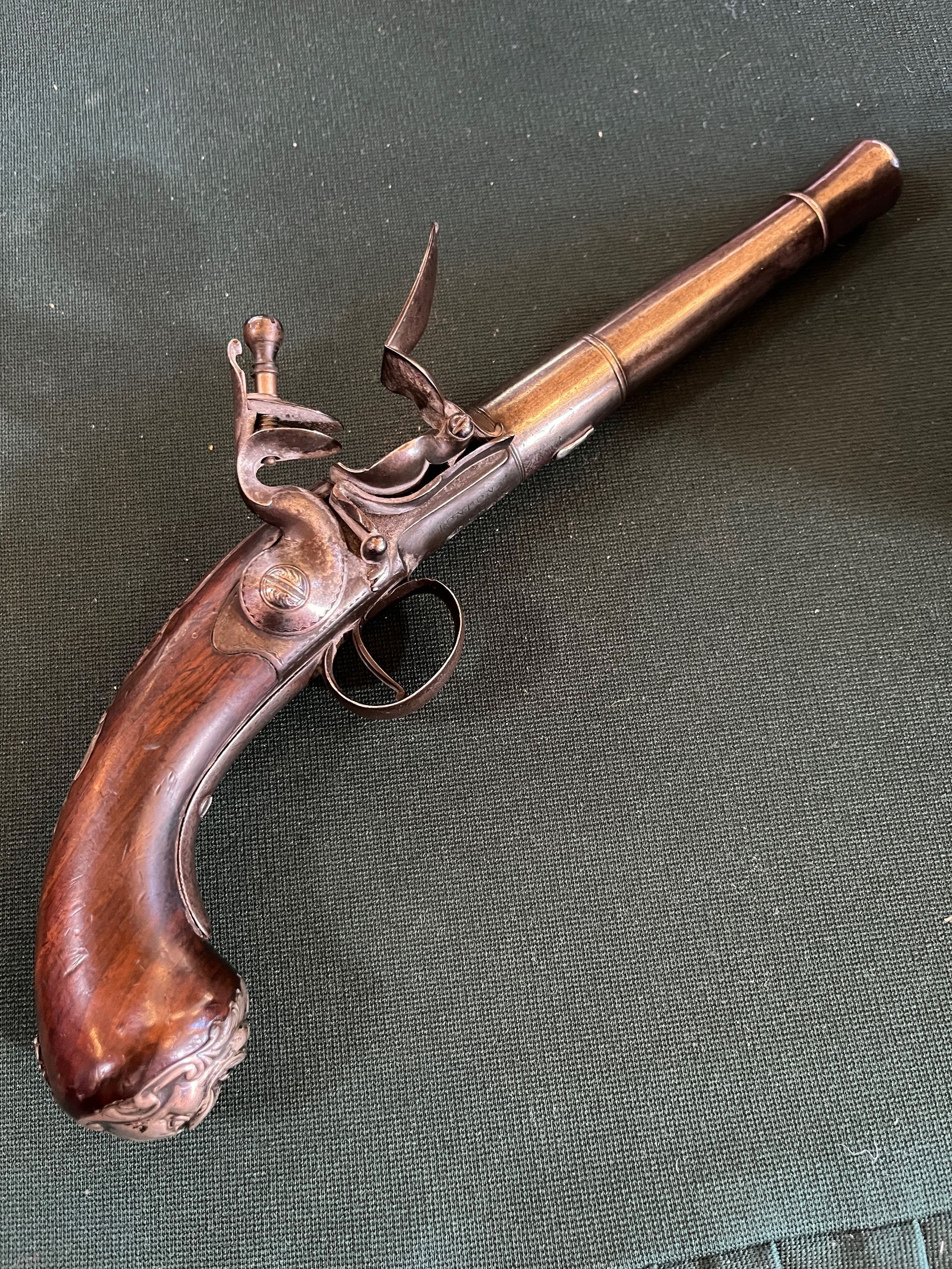 Antique flintlock pistol with a wooden handle on a green surface.