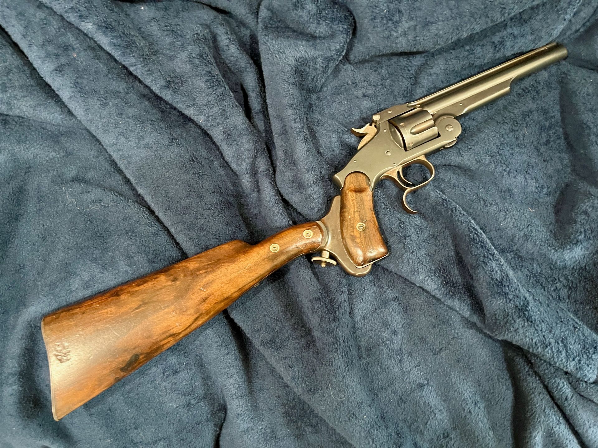 Antique revolver with wooden shoulder stock on a dark blue fabric.