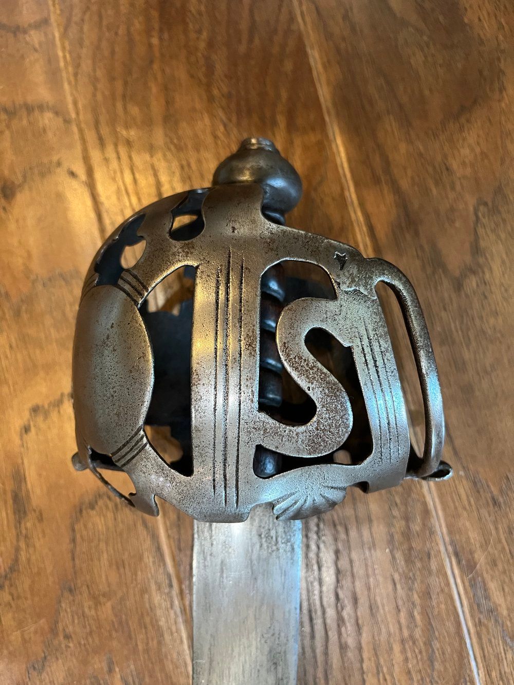 Close-up of a sword hilt with a decorative, openwork guard featuring the initials 