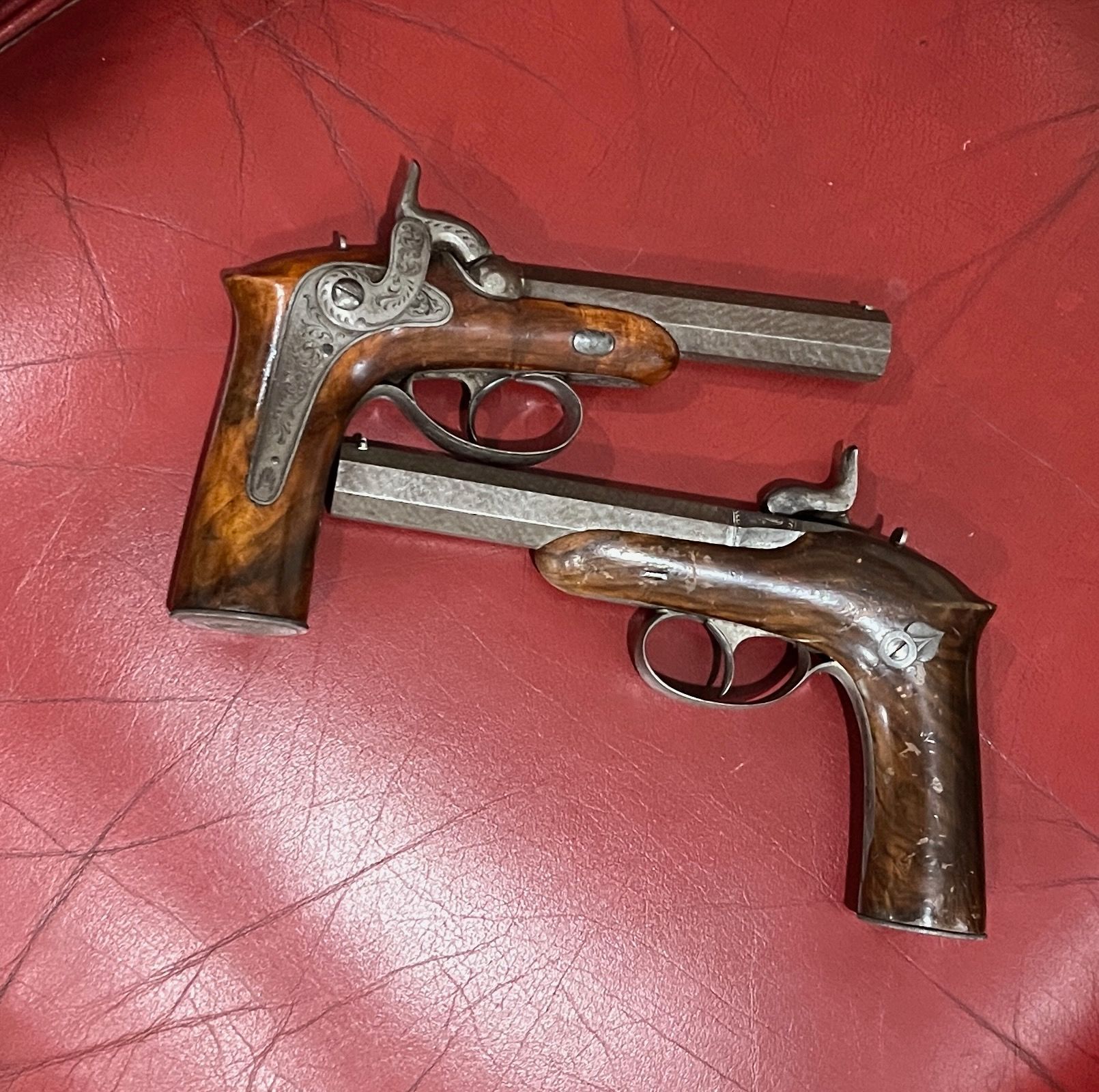 Two antique, wooden-handled pistols on a red surface.
