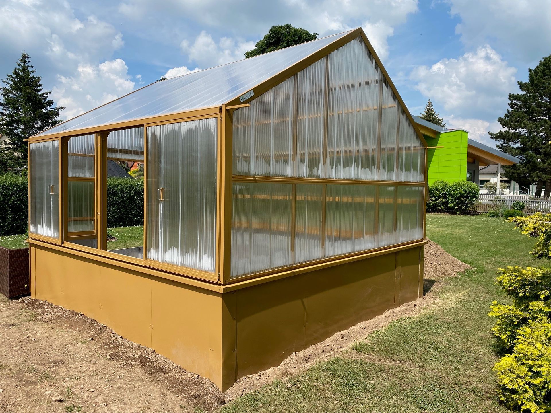 Ein gelbes freistehendes Gewächshaus mit Hochbeete und Bodenbeete innen, 4x4m groß.