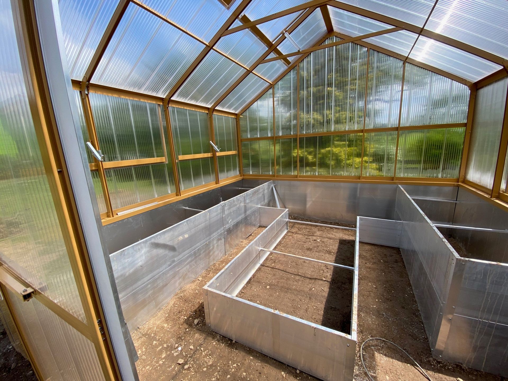 Ein gelbes freistehendes Gewächshaus mit Hochbeete und Bodenbeete innen, 4x4m groß.