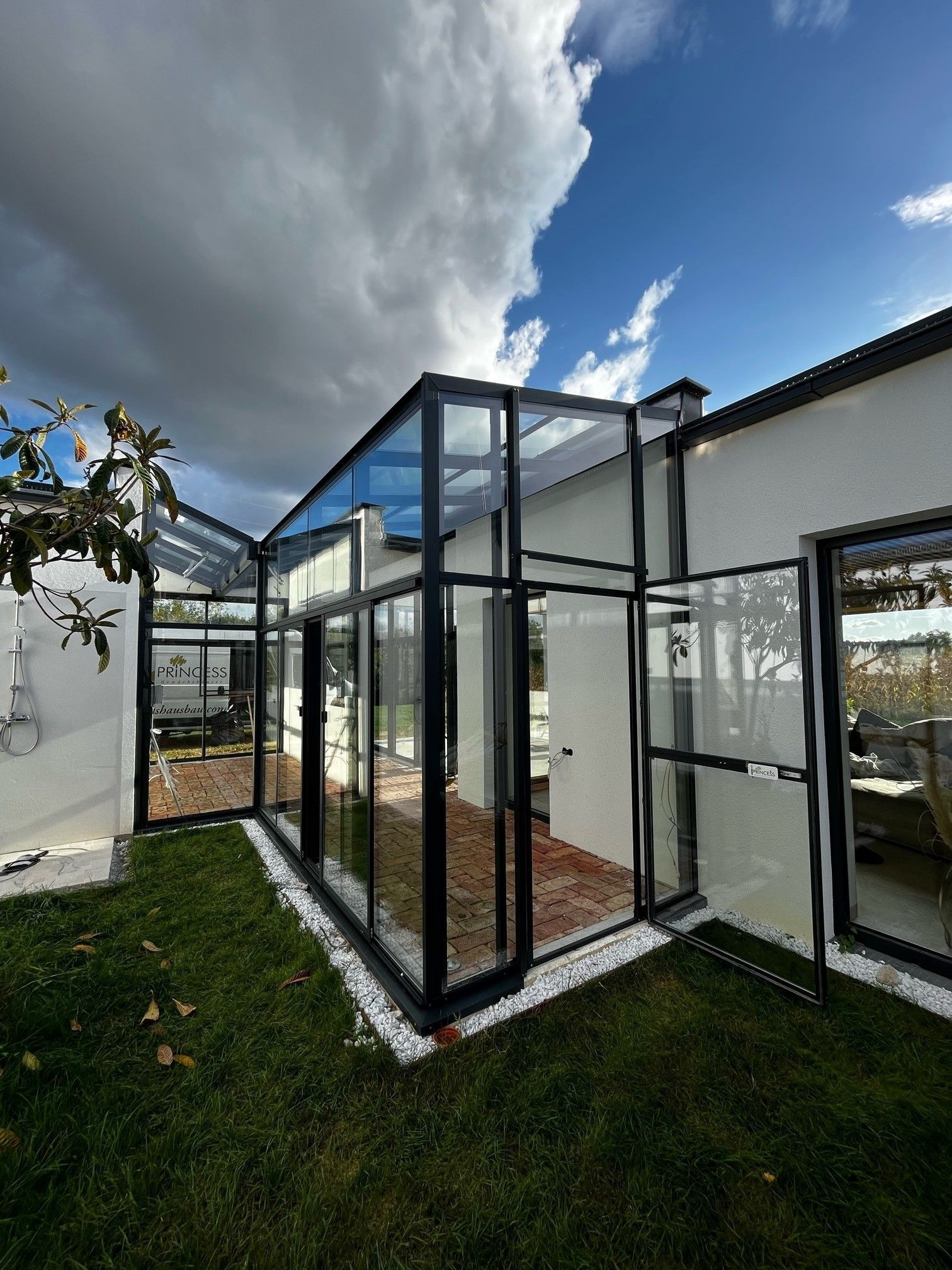 Orangerie - Pultdach Gewächshaus zwischen zwei Gebäuden eingabaut. Komplett in Echtglasausführung, Gerüst in schwarzer Farbe. Größe 3x7,7m.