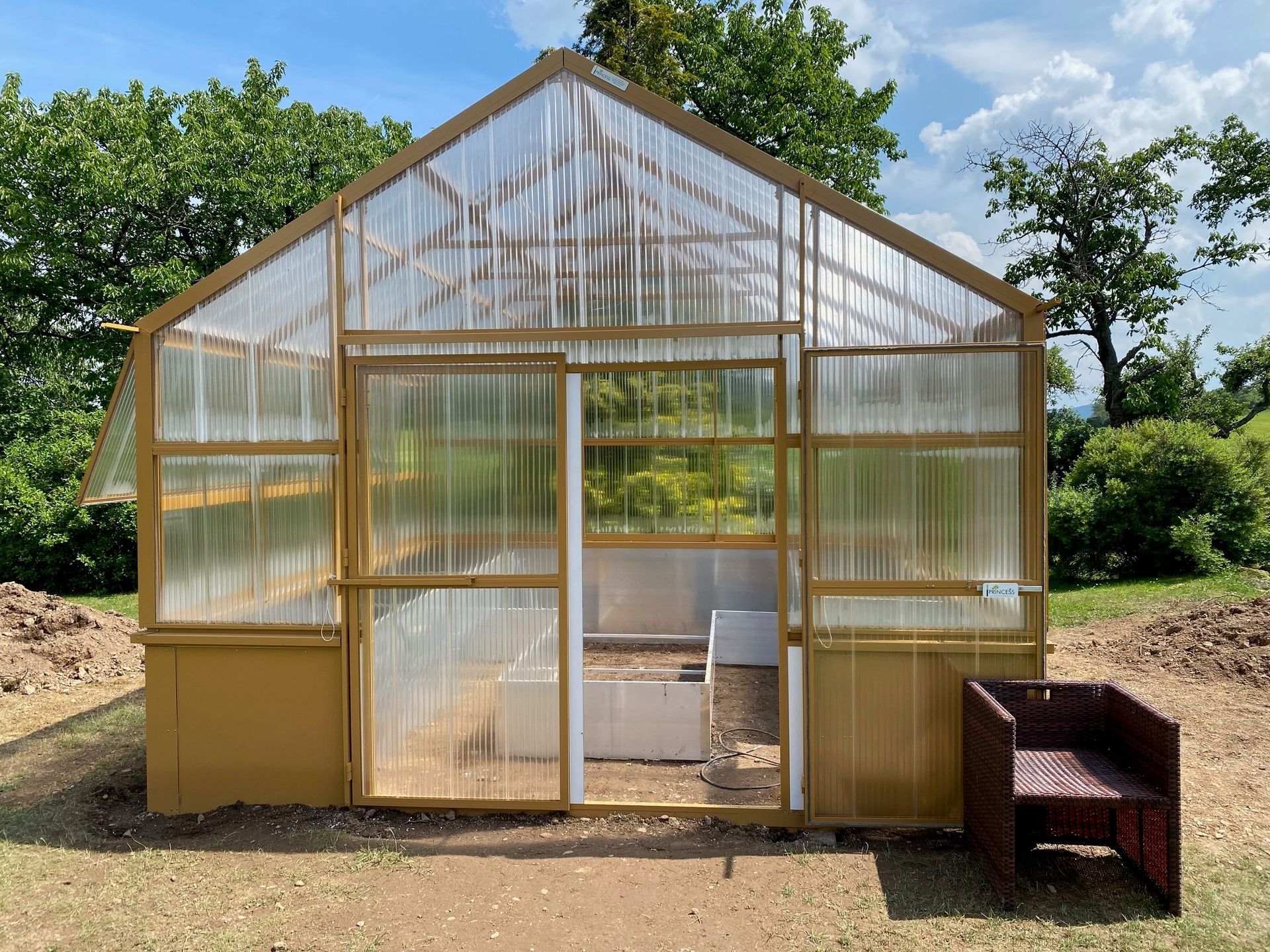 Ein gelbes freistehendes Gewächshaus mit Hochbeete und Bodenbeete innen, 4x4m groß.