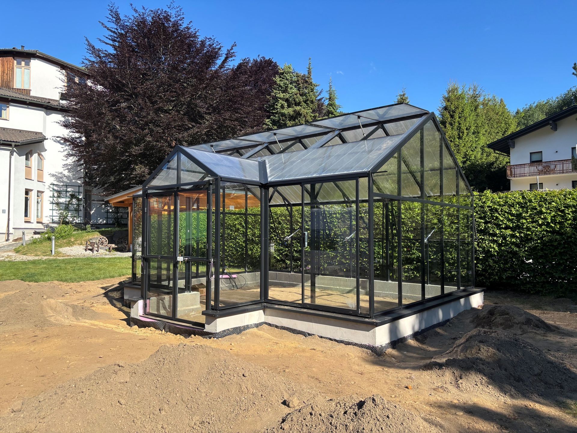 Freistehendes Gewächshaus mit Satteldach und Graupe. Haupttrakt 4,5x6m, Graupe 2x1m. Seitenwände in Echtglasausführung. Gerüst in schwarze Farbe.