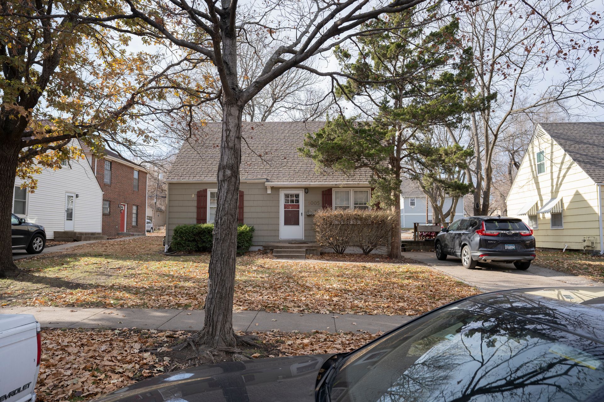 Small house with a brown roof and red door, flanked by trees. Cars are parked in front.