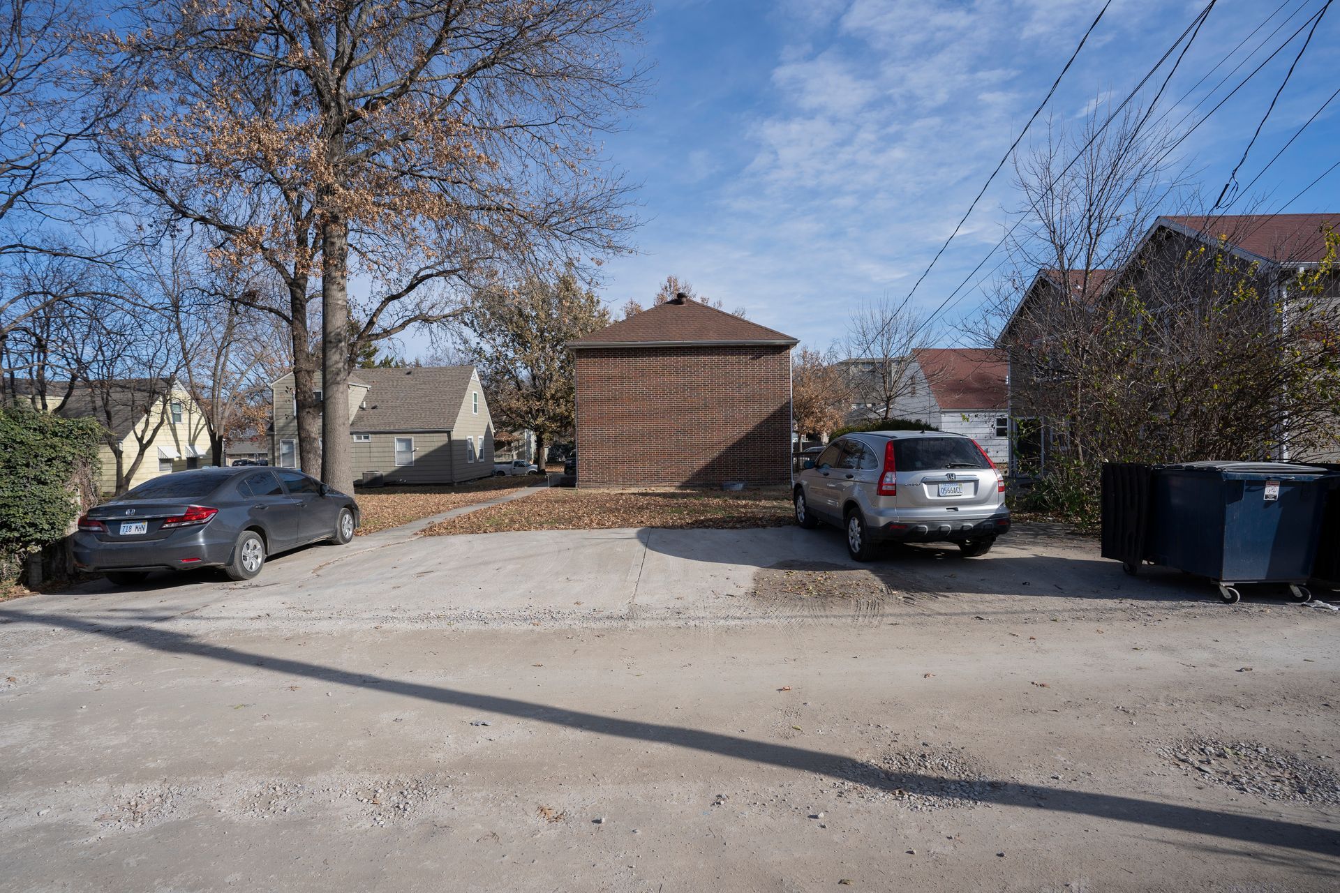 Gravel parking area with two cars, a brick building, and houses on a sunny day.