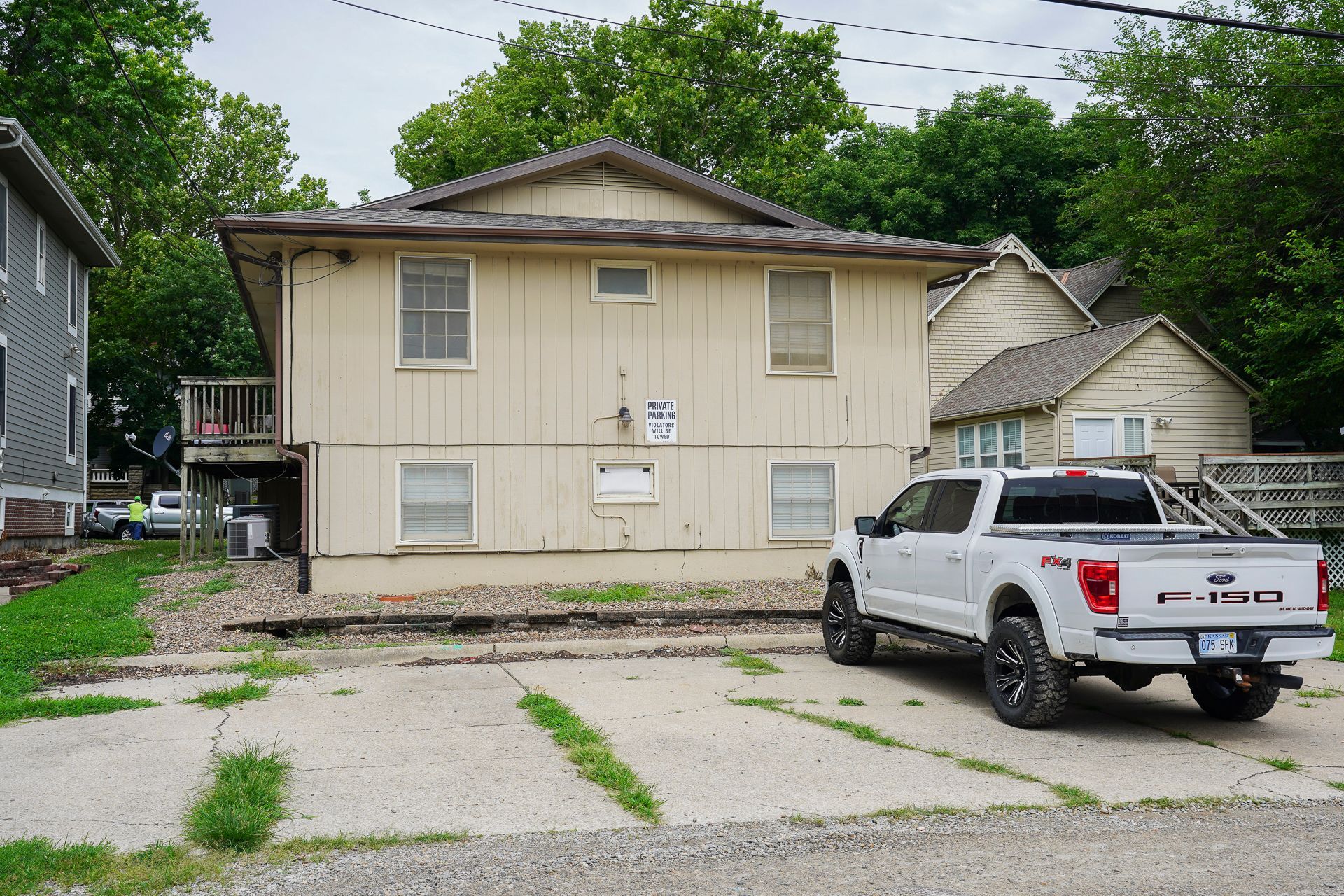 Two-story beige house with a white truck parked in front on a gravel and concrete driveway.