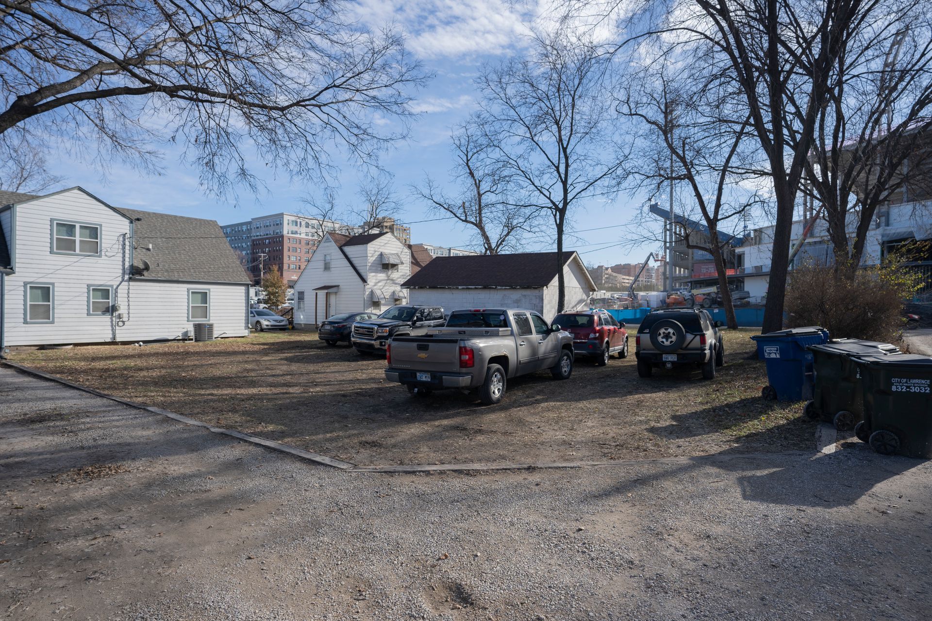 Parking lot with several cars, including a pickup truck, in front of small houses on a sunny day.