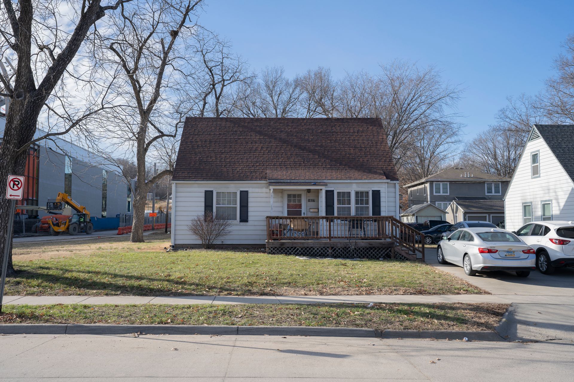White bungalow with brown roof and small porch; cars parked in driveway.