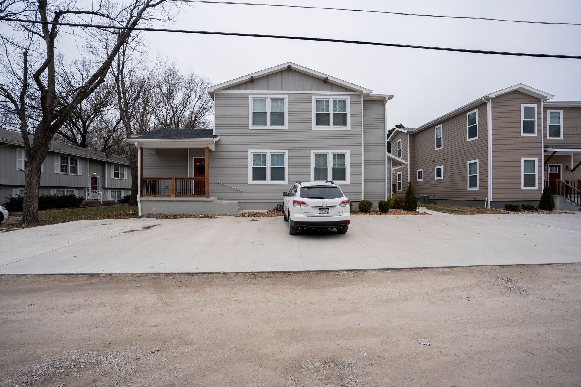 Light grey multi-unit building with a car parked in front. Overcast sky, a few trees.