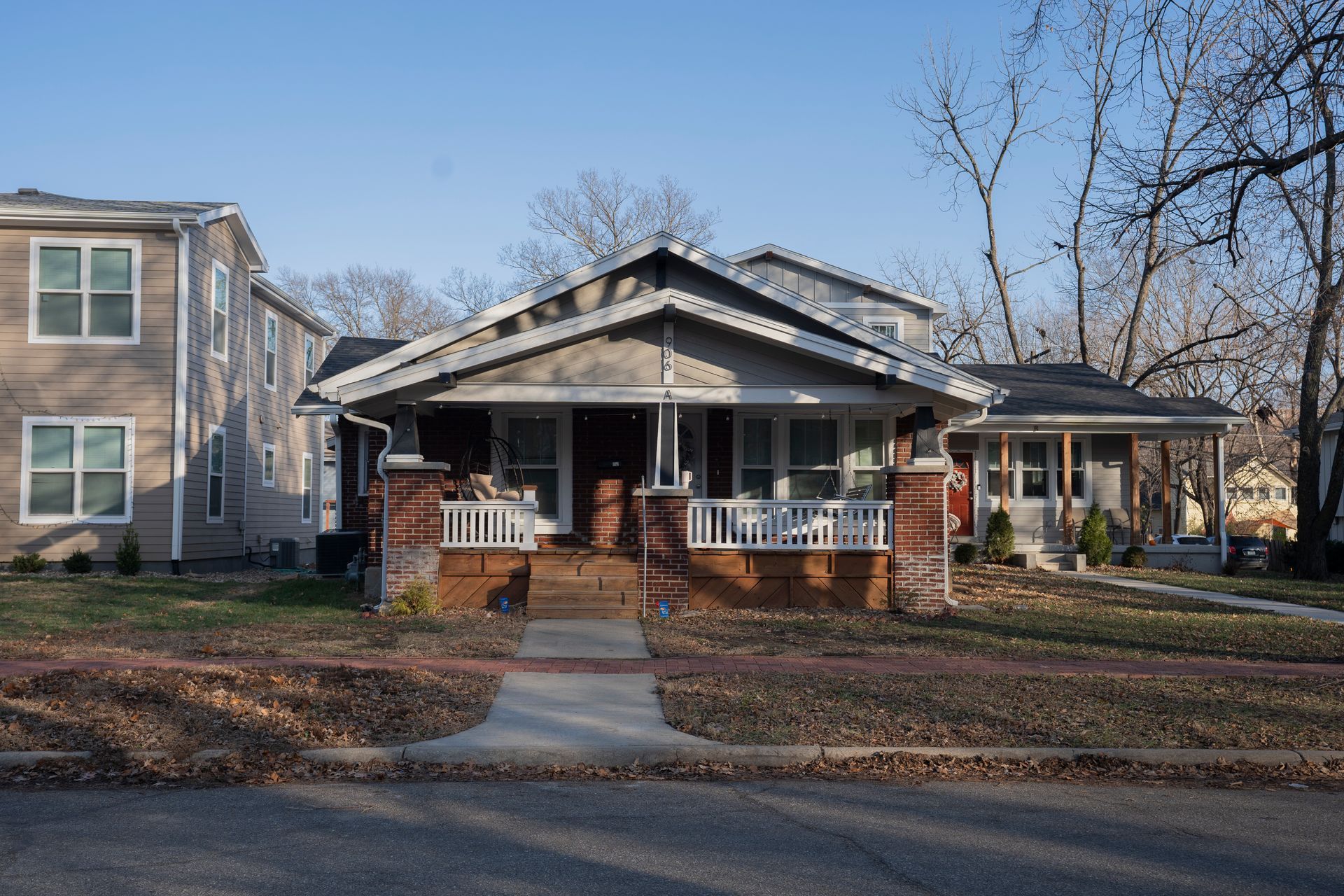 Craftsman-style home with porch; brick stairs, neutral siding. Sunny day, bare trees, sidewalk in front.