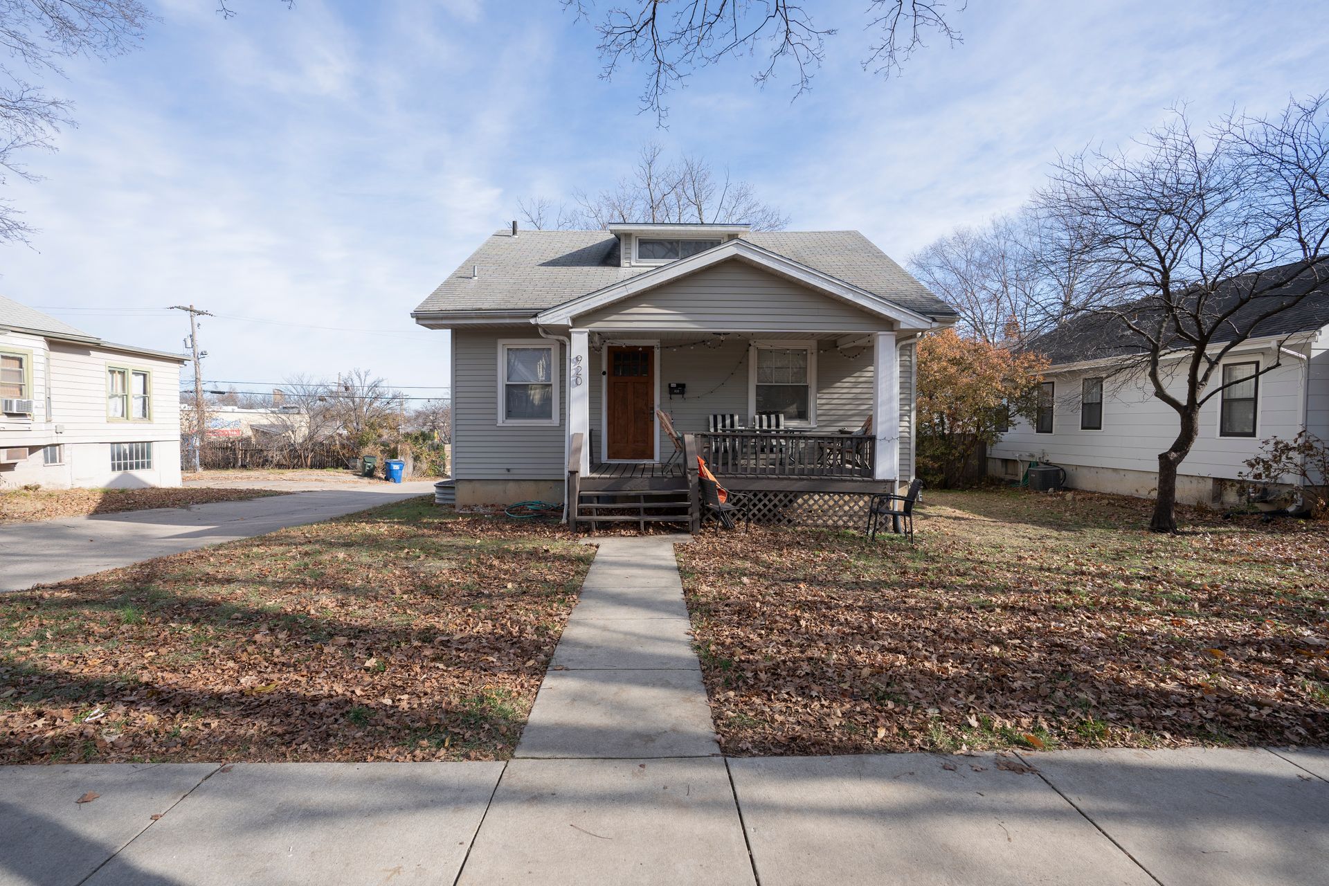 Small gray house with porch and sidewalk; fallen leaves on lawn.