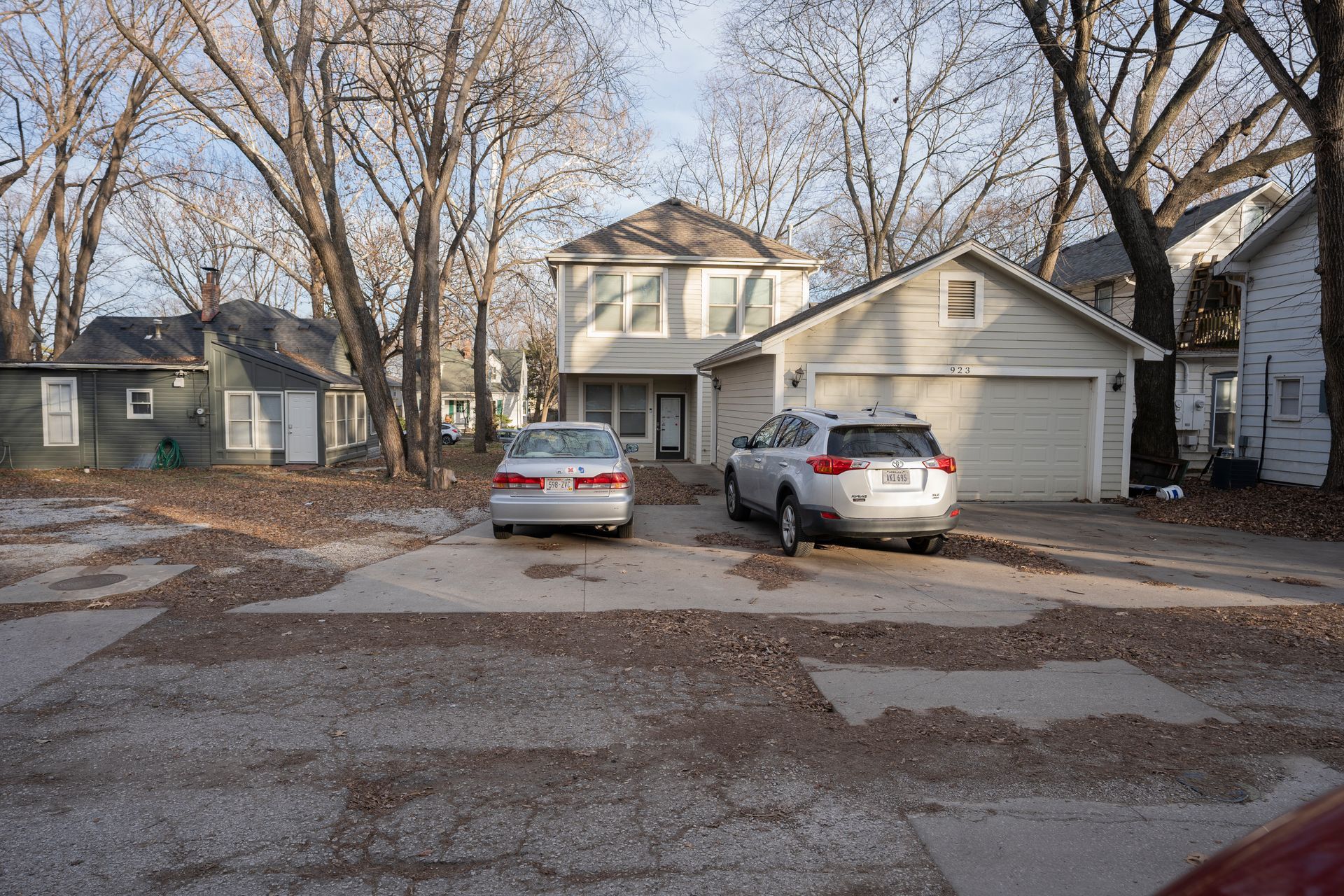 Two-story house with attached garage, two cars parked in front, surrounded by leafless trees.