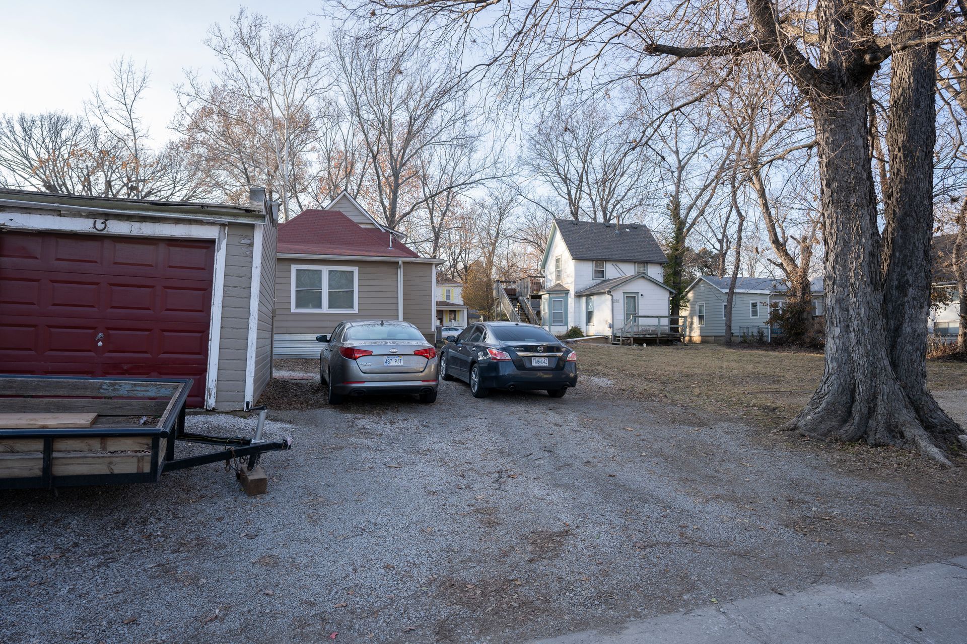 A gravel driveway with two cars parked in front of a small house and garage on a sunny day.