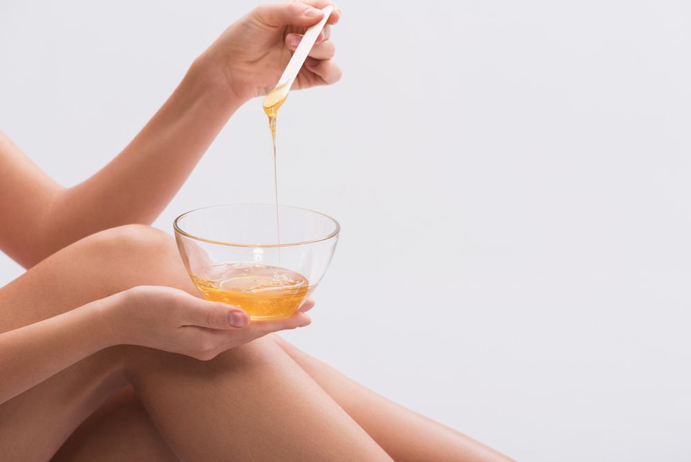 Hands Pouring Yellow Liquid Into a Clear Bowl Held Over a Bare Leg — Villa Nails & Beauty in Airlie Beach, QLD
