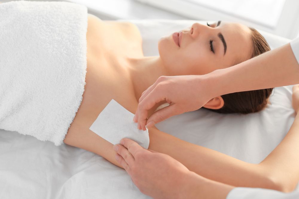 Hand Applying Wax Strip to A Woman Underarm During a Waxing Treatment — Villa Nails & Beauty in Cannonvale, QLD