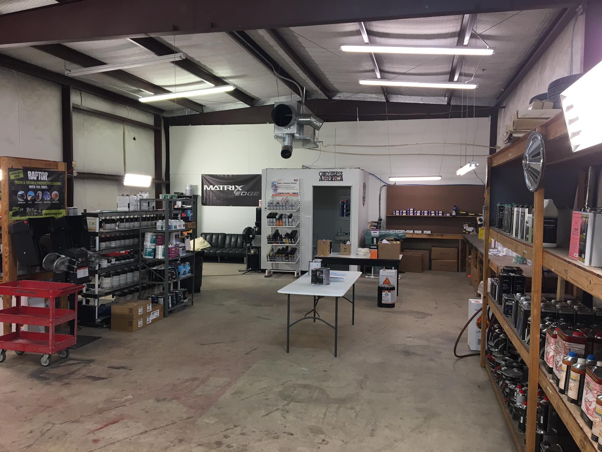 Interior of a retail space, with shelves of merchandise and a central table. White walls, industrial lighting.