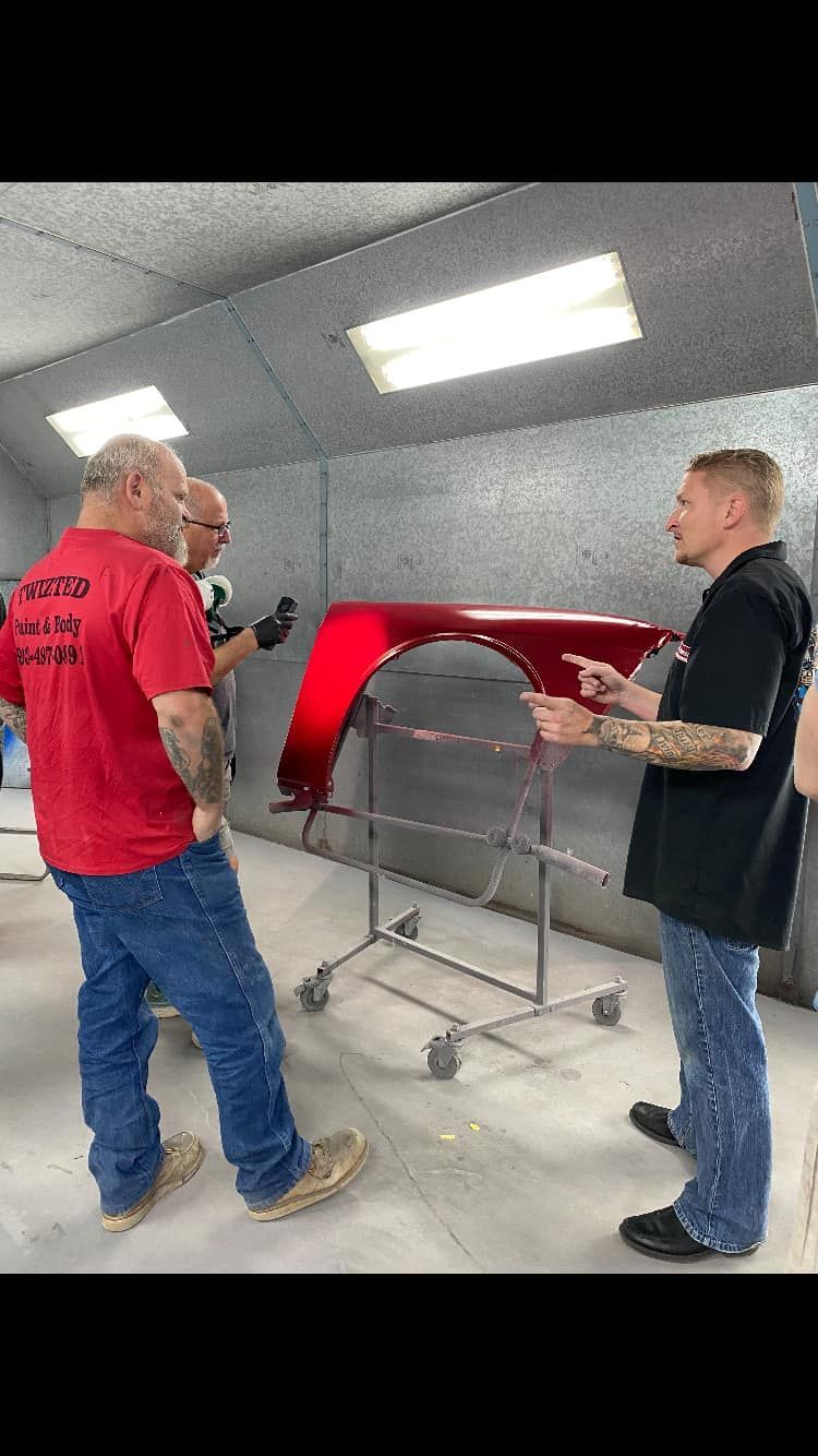Three men in a paint booth examining a freshly painted red car panel.