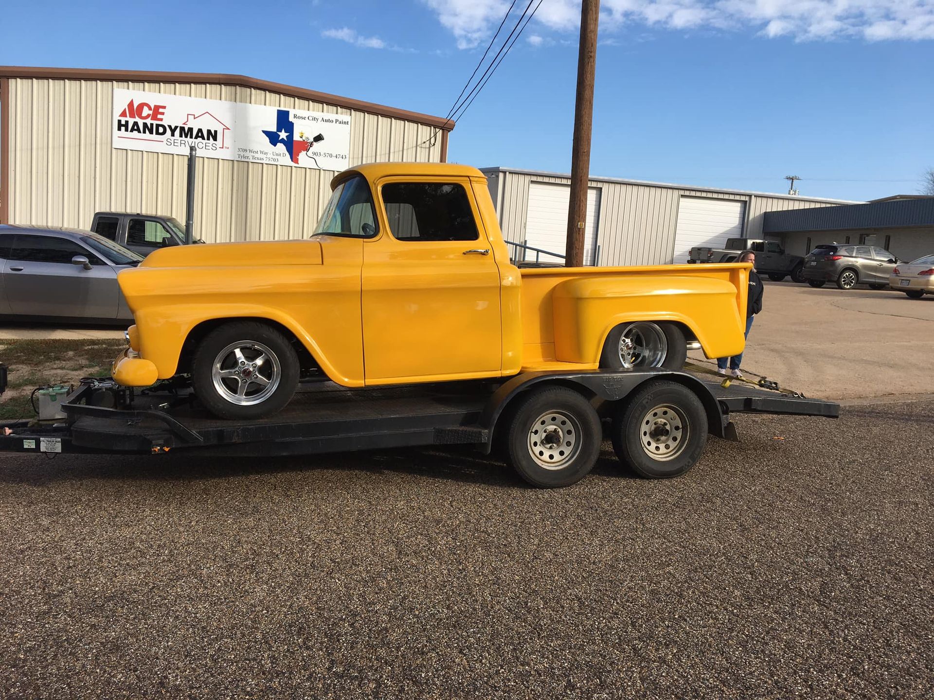Yellow vintage truck on a trailer in front of Ace Handyman store.