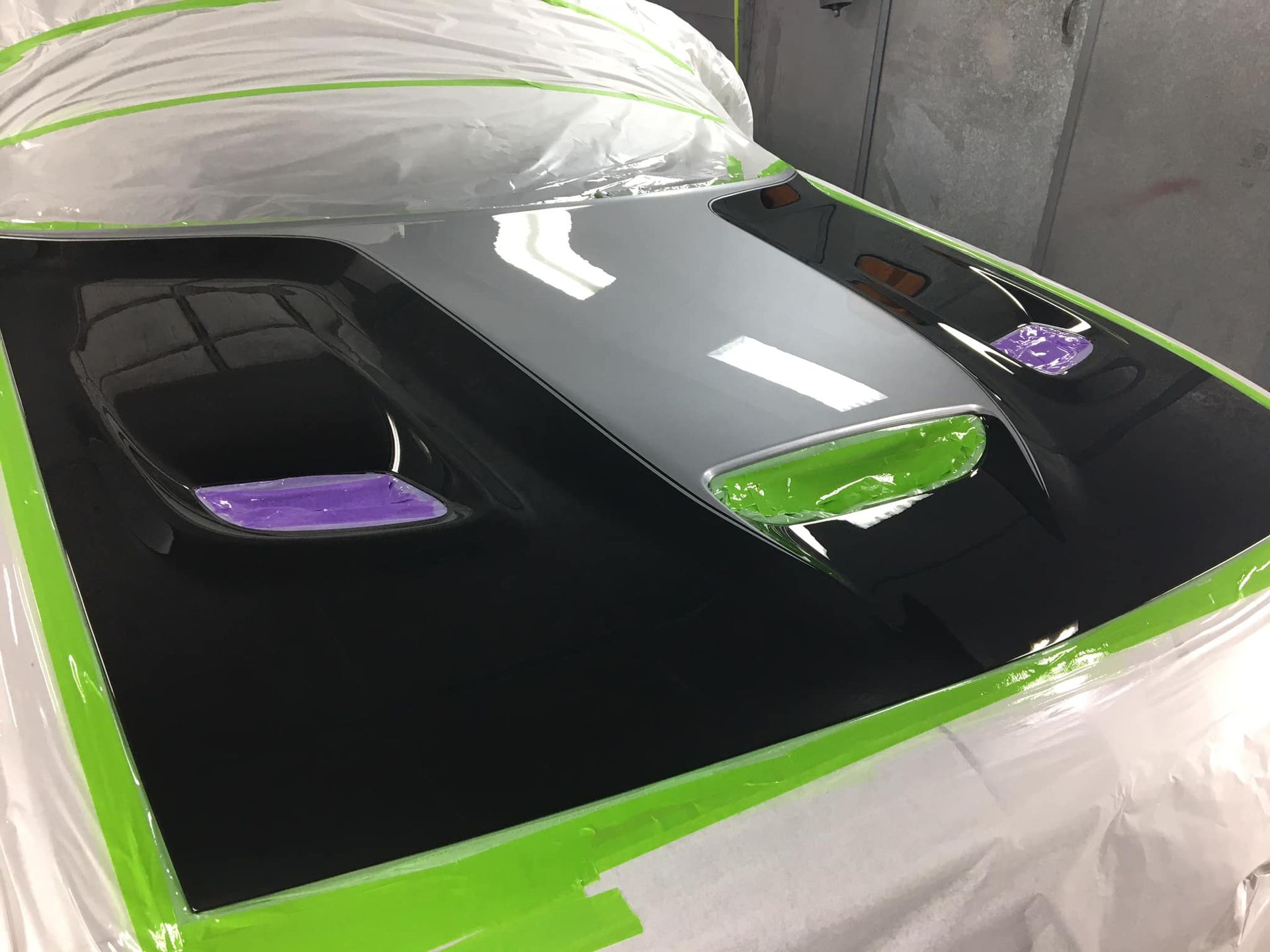 Black car hood with green-masked edges, purple and green accent details, and clear plastic covering.